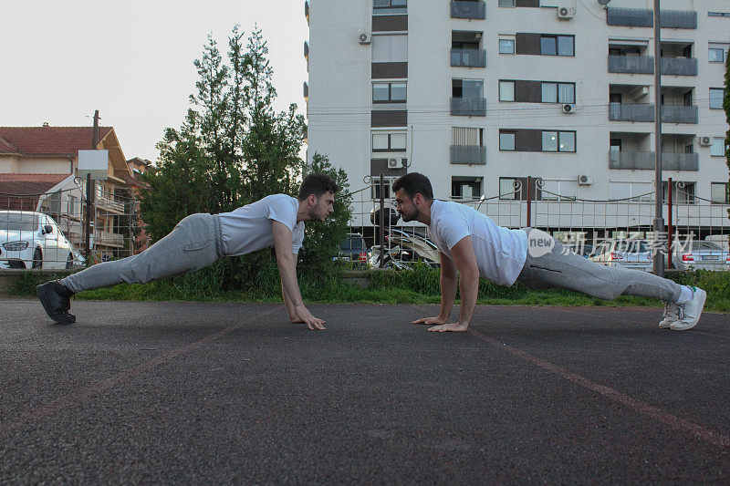 Two white men doing pushups together in a public park